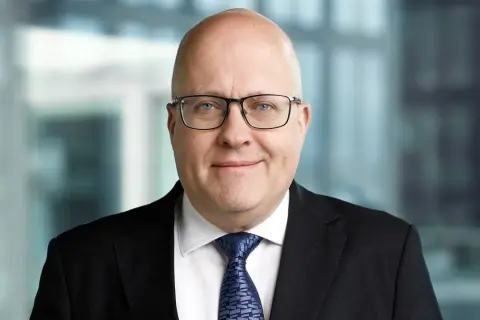 Mikael Staffas, en man med glasögon och kostym, ler mot kameran.