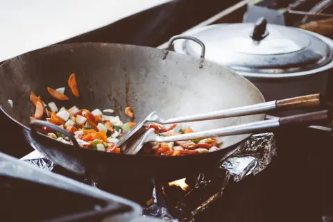 Wok med grönsaker som steks, med olika peppar sorter som ger smak. En gryta står i bakgrunden.