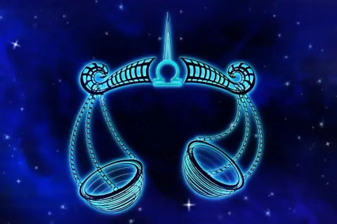 Błękitna waga symbol zodiaku, jakby zrobiona z kamieni szlachetnych, unosi się na tle nocnego nieba pełnego gwiazd.