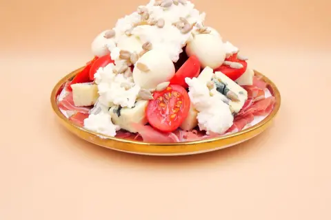 Sałatka z szynką parmeńską, serami, pomidorkami i słonecznikiem na złotym talerzu.