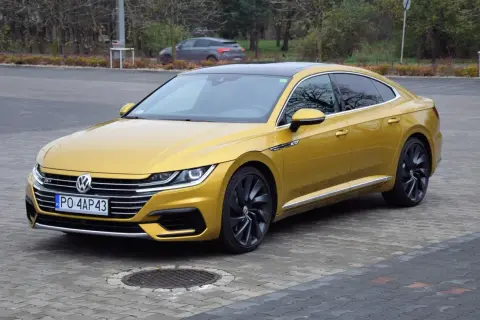 Złoty Volkswagen Arteon R z czarnym dachem i felgami, zaparkowany na bruku.