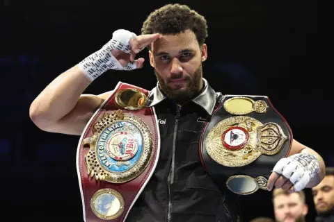A boxer, champion of the super flyweight weight class, salutes with his championship belts.