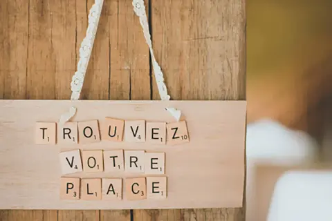 Marque place bouchon liège DIY : "Trouvez votre place" écrit avec des lettres Scrabble sur une planche en bois.
