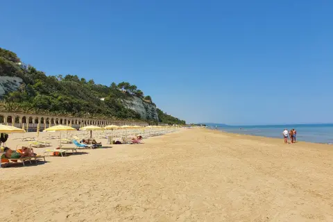 Spiaggia di ponente Rodi Garganico: sabbia dorata, ombrelloni gialli e un mare azzurro sotto un cielo limpido.