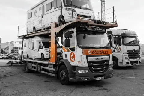 Camión transportando caravanas, dos vehículos recreativos apilados listos para su transporte.