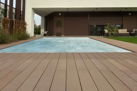 Ponte in legno effetto grana, ideale per esterni, circonda una piscina coperta. I requisiti dei pavimenti per esterni sono soddisfatti da questo materiale resistente e bello.