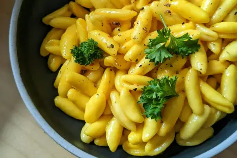 Żółty makaron gnocchi w sosie, udekorowany natką pietruszki i pieprzem, w ciemnej misce.