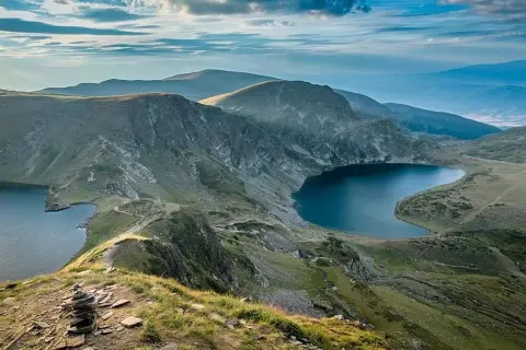 Vue panoramique d'un trek en Bulgarie. Des lacs glaciaires d'un bleu profond bordent des montagnes verdoyantes sous un ciel nuageux.