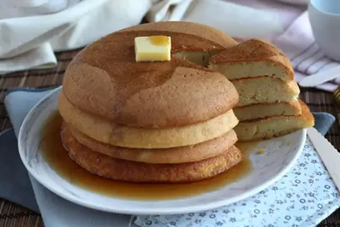 En hög med fluffiga japanska pannkakor, toppad med smör och sirap, serveras på en tallrik.