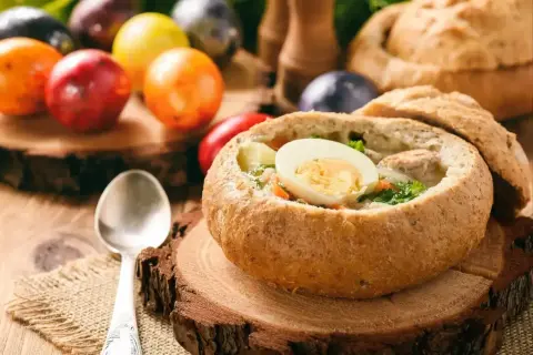 Pyszny barszcz biały lub żurek w chlebie, ozdobiony jajkiem. W tle kolorowe pisanki i bochenek chleba.