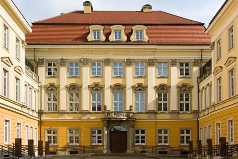 Elegancki budynek z żółtą fasadą i czerwonym dachem, ozdobiony licznymi oknami. To muzeum sztuki medalierskiej we Wrocławiu.