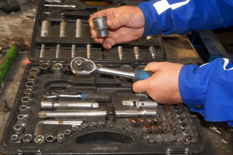 Wybieranie odpowiednich rozmiarów grzechotek z walizki narzędziowej. Ręce mechanika w niebieskim kombinezonie trzymają klucz i nasadkę.