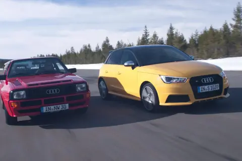 Dwa Audi S1 Quattro, czerwony klasyk i żółty współczesny, pędzą po drodze wśród zimowych krajobrazów.