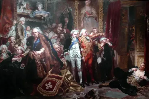 Obraz przedstawia scenę z życia **sarmatów**. W centrum grupa mężczyzn w barwnych strojach, jeden wskazuje palcem, inny leży na ziemi.