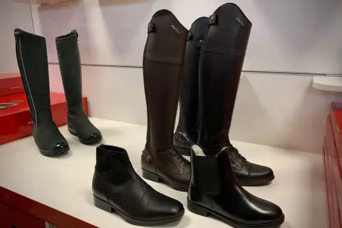 Kozaki jeździeckie, botki i inne buty do jazdy konnej prezentowane na białej półce.
