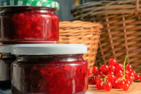 Słoiki z domowym dżemem z porzeczki czerwonej, obok świeże owoce. W tle plecione kosze.