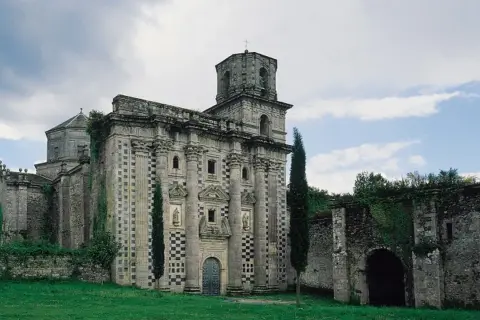 El imponente monasterio de Monfero, con su fachada de piedra y torre octogonal, se alza entre la vegetación, evocando historias de tiempos pasados.