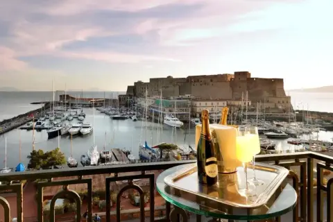 En balkong med champagne och glas, med en vy över hamnen och Castel Nuovo i Neapel.