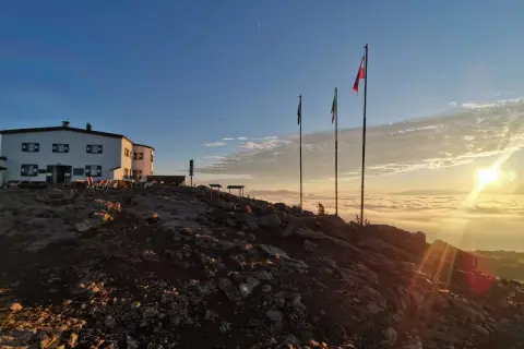Sonnenaufgang über einer Wolkendecke, mit Hütte und Fahnen. Ein perfekter Moment auf der Sarntaler Hufeisentour.