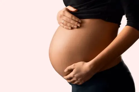 Schwanger und besorgt wegen eines Bandscheibenvorfalls? Die Hände einer Frau stützen sanft ihren runden Bauch.