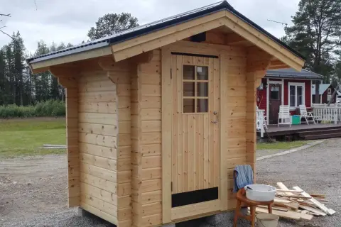 Nybyggt utedass i trä, redo att användas. Enkla verktyg och material ligger redo för att bygga utedass.
