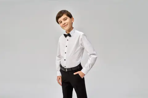 Chłopiec w eleganckiej białej koszuli z czarną muszką i spodniach. Idealny strój, co na komunie dla chłopca.