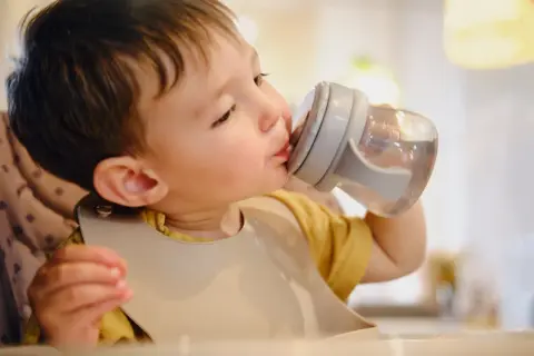 Un petit garçon boit de l'eau dans une tasse à bec, assurant son hydratation bébé.