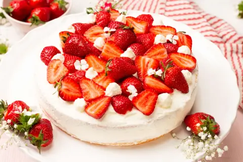 Eine köstliche Erdbeer-Sahne-Torte, üppig belegt mit frischen Erdbeerscheiben und Sahnetupfern, verziert mit kleinen weißen Blüten.