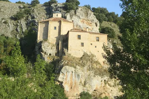 Edificio de piedra en un acantilado, rodeado de vegetación. Podría ser el lugar dónde nació Antonio Machado.