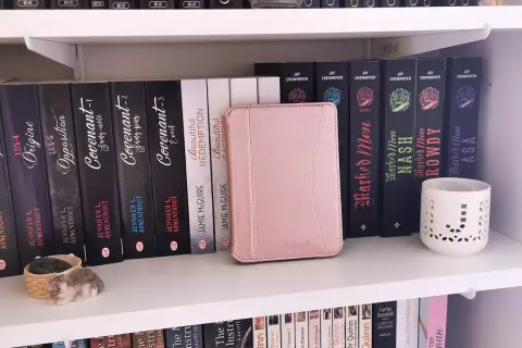 Une liseuse Kobo rose est bloquée en veille, posée sur une étagère remplie de livres.