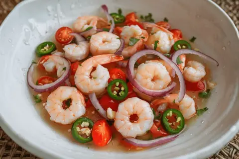 Un refrescante ceviche de gambas con tomate, cebolla morada y jalapeño en un cuenco blanco.