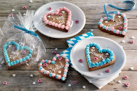 Bunte Lebkuchenherzen selber machen: mit Zuckerguss und Sprüchen verziert, liegen sie auf Holztisch.