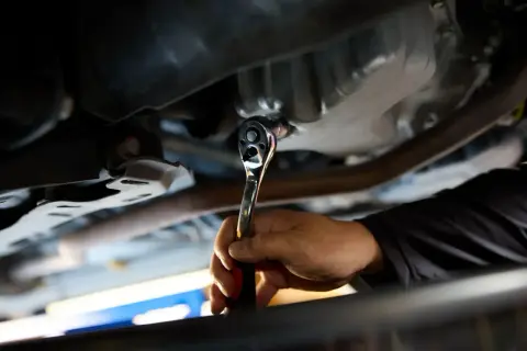 Dłoń mechanika dokręca kluczem nasadowym korek spustowy oleju. Ważne jest, z jaką siłą dokręcać korek spustowy oleju, by nie uszkodzić miski olejowej.