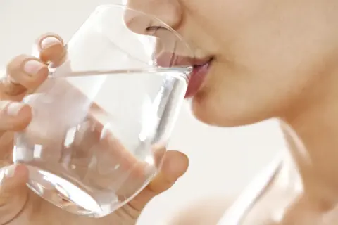 Une femme boit un verre d'eau. Une question importante pour les jeunes mamans : quelle eau boire allaitement ?