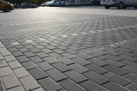 Szary parking wyłożony kostką holland. W tle widać zaparkowane samochody.