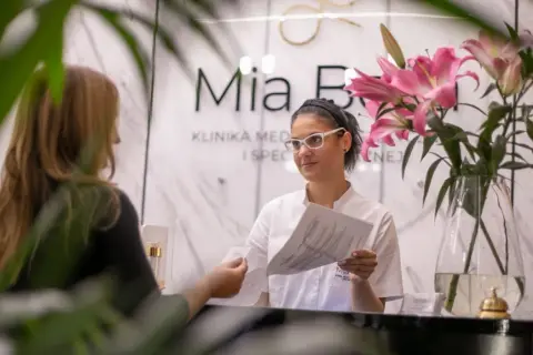 Recepcjonistka w klinice dermatologii estetycznej podaje dokument pacjentce.