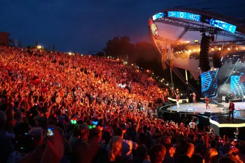 Tłumy rozbawionych ludzi na mrągowo festiwal, oświetlone sceną i kolorowymi światełkami.