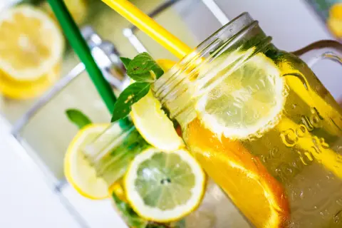 Jak zrobić lemoniadę? Orzeźwiający napój z cytryną, pomarańczą i miętą w słoiku z uchwytem, ozdobiony plasterkami owoców i zielonymi słomkami.