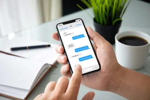 Dłoń trzyma smartfon z otwartą aplikacją do wiadomości tekstowych, na ekranie widoczna jest konwersacja.