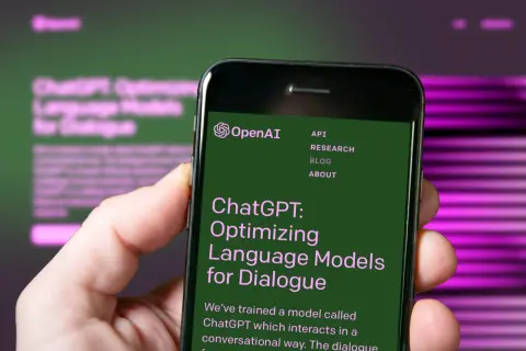 Dłoń trzyma smartfon z otwartą stroną OpenAI, prezentującą ChatGPT: Optymalizację modeli językowych do dialogu.