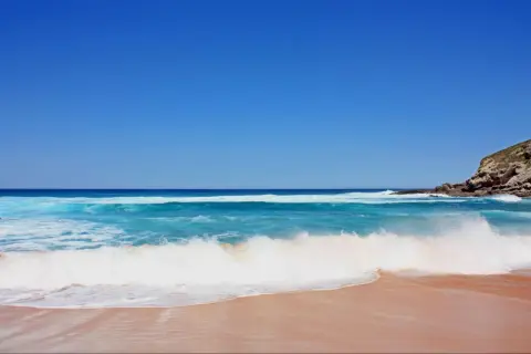Olas rompiendo en una playa de arena dorada, ideal para saber donde hacer snorkel en Cantabria. Cielo azul intenso.