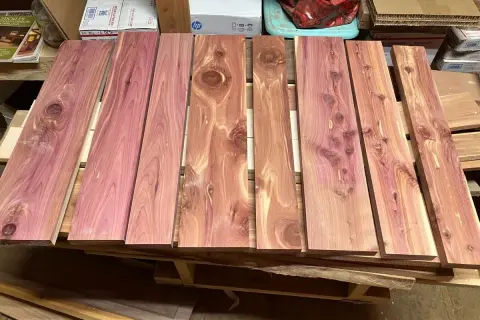 Tablones de madera de enebro con vetas rosadas y nudos visibles, apilados sobre un palé.