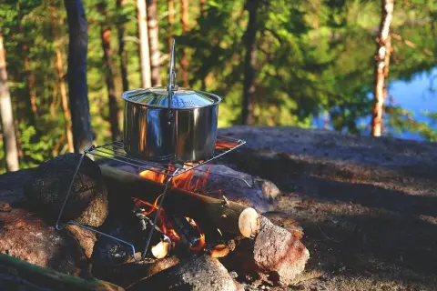 Olla de metal sobre una parrilla encima de una fogata, lista para cocinar. Un bushcrafter prepara su comida en la naturaleza.