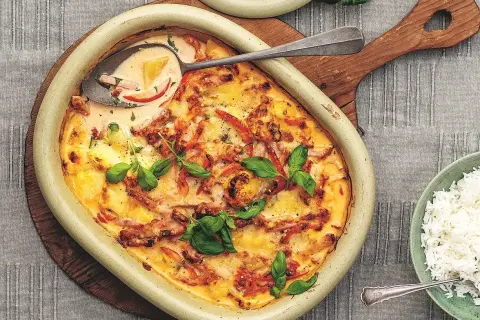En gratinerad kassler med ananas i en ugnsform, toppad med färska örter. Serveras med ris.