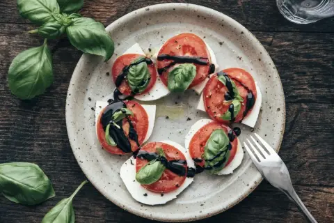 Tomate-Mozzarella-Salat mit frischem Basilikum und Balsamico-Glasur auf einem rustikalen Teller.