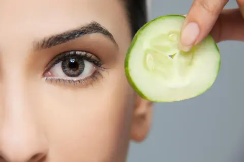 Une tranche de concombre est tenue près de l'œil, une méthode naturelle pour enlever les poches sous les yeux.