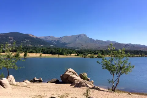 Tranquilo embalse de Navacerrada con montañas al fondo y rocas en la orilla.