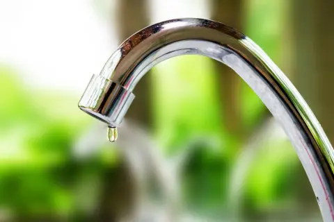 Close-up of a dripping chrome faucet with a water droplet forming.