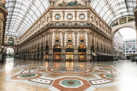 Ett tomt, lyxigt modehus i Milano med en vacker mosaikgolv och glastak. Louis Vuitton-butiken lyser upp.
