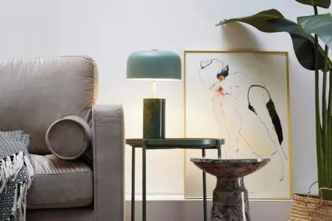 Stylowa lampa metalowa z zielonym kloszem i marmurową podstawą, obok kanapy i obrazu.